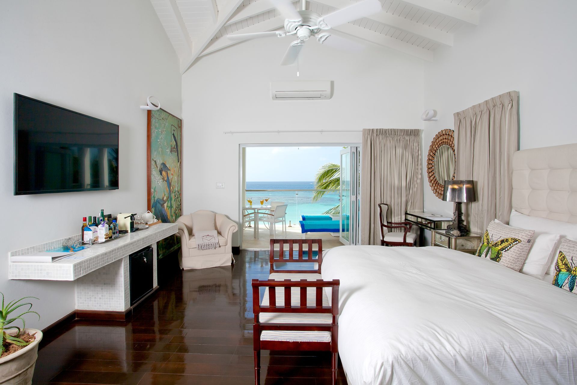 Bedroom with a large bed, a wall-mounted TV, and open doors leading to the ocean.