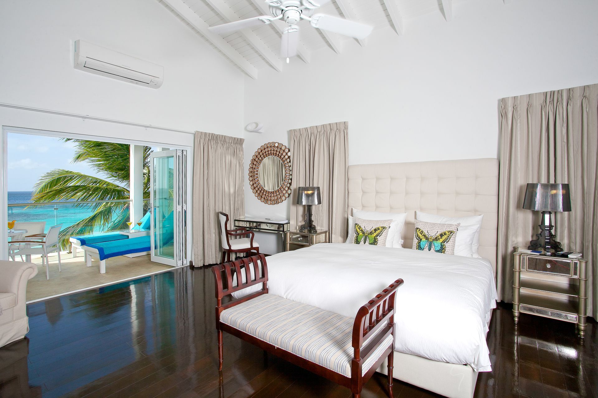 Bedroom with a bed, ocean view, open doors, white walls, and dark wood floor.