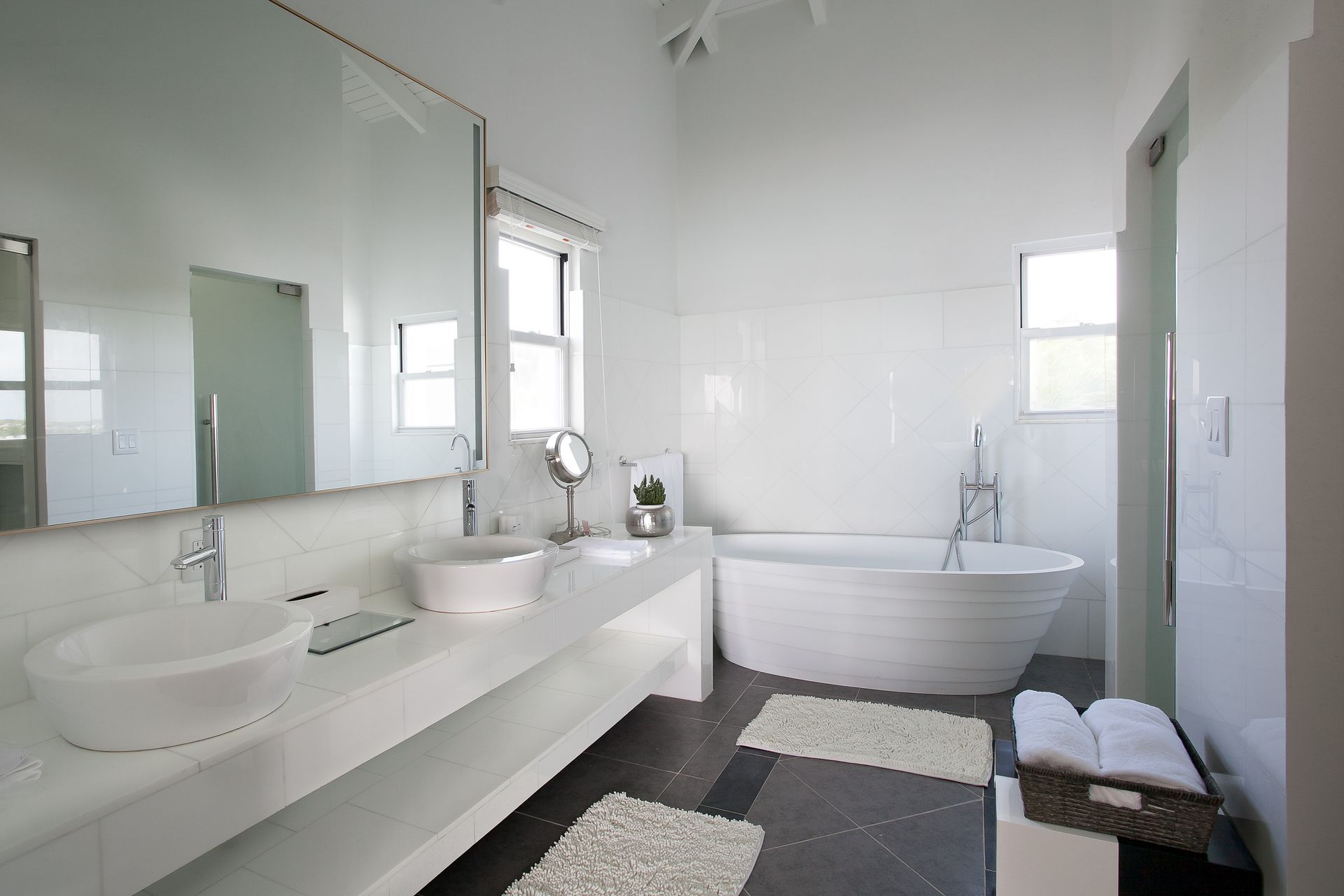White bathroom with a free-standing tub, double sinks, and white tile walls.