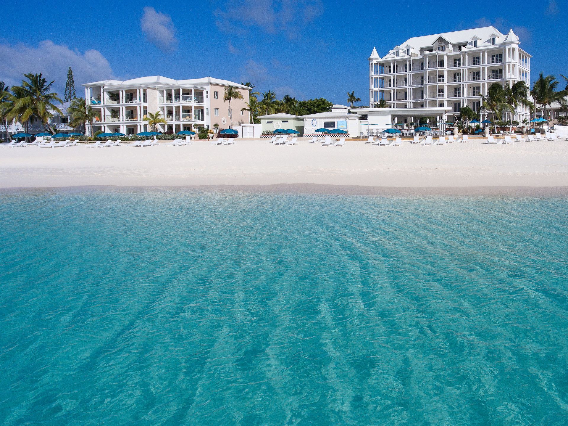 White sand beach with turquoise water, white buildings in the background, sunny day.