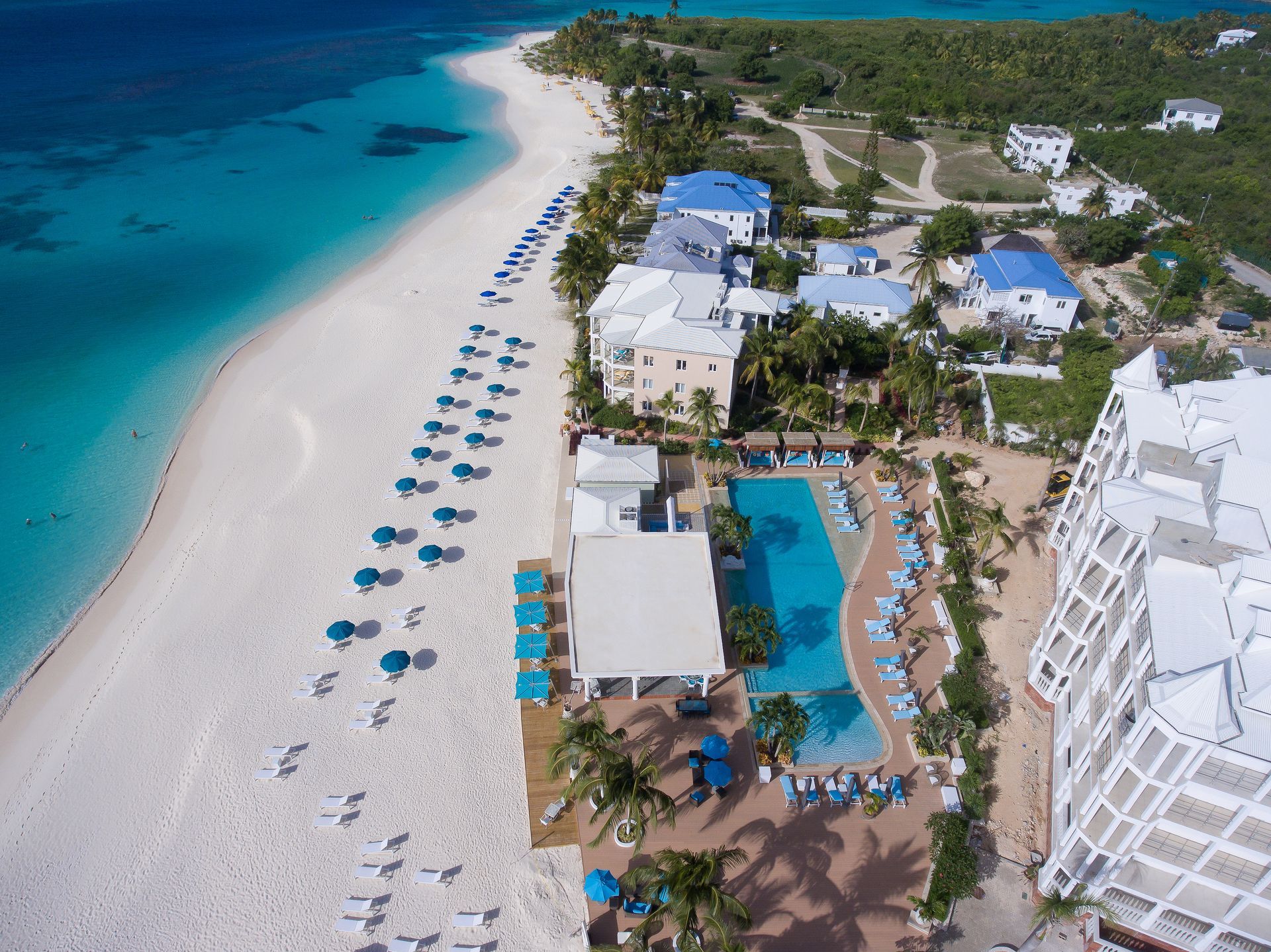 Aerial view of a white sand beach with turquoise water, resort buildings, and umbrellas.