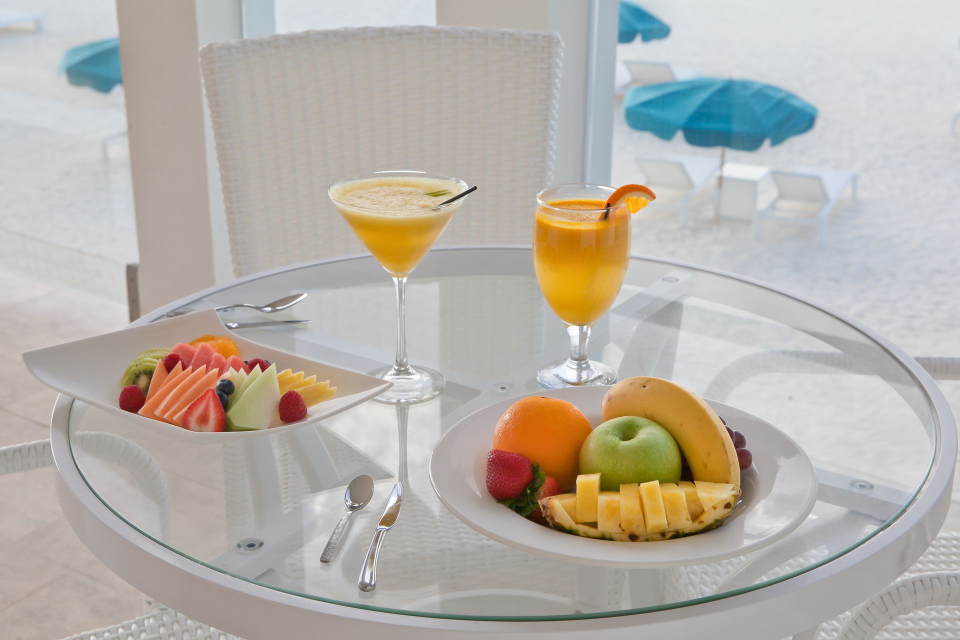 Table with fruit, cocktails, and beach view.