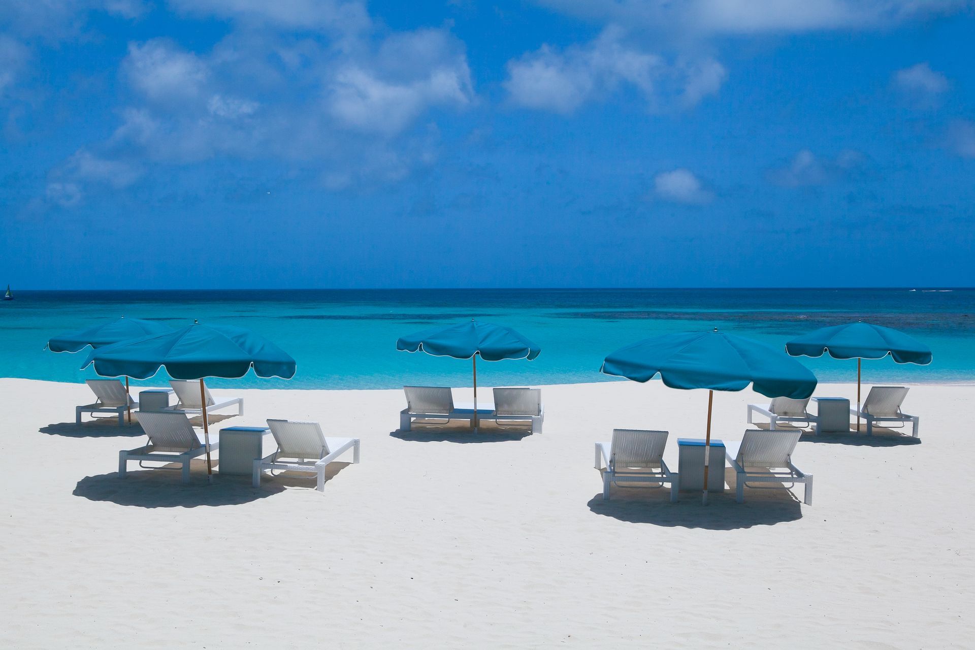White sand beach with teal umbrellas and lounge chairs under a blue sky.