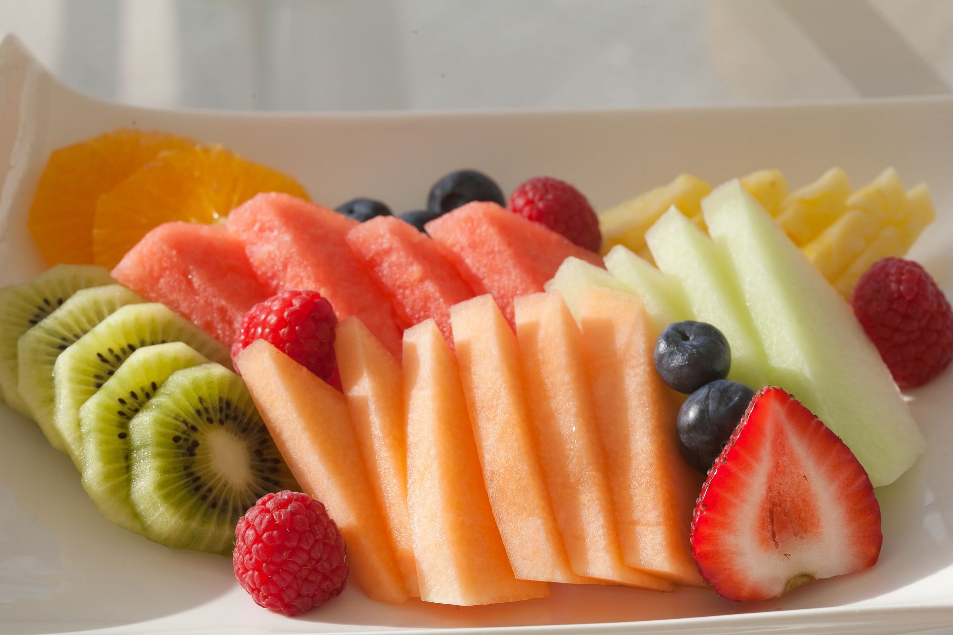 Sliced fruit platter: orange, kiwi, cantaloupe, watermelon, honeydew, raspberries, blueberries, strawberry, pineapple.