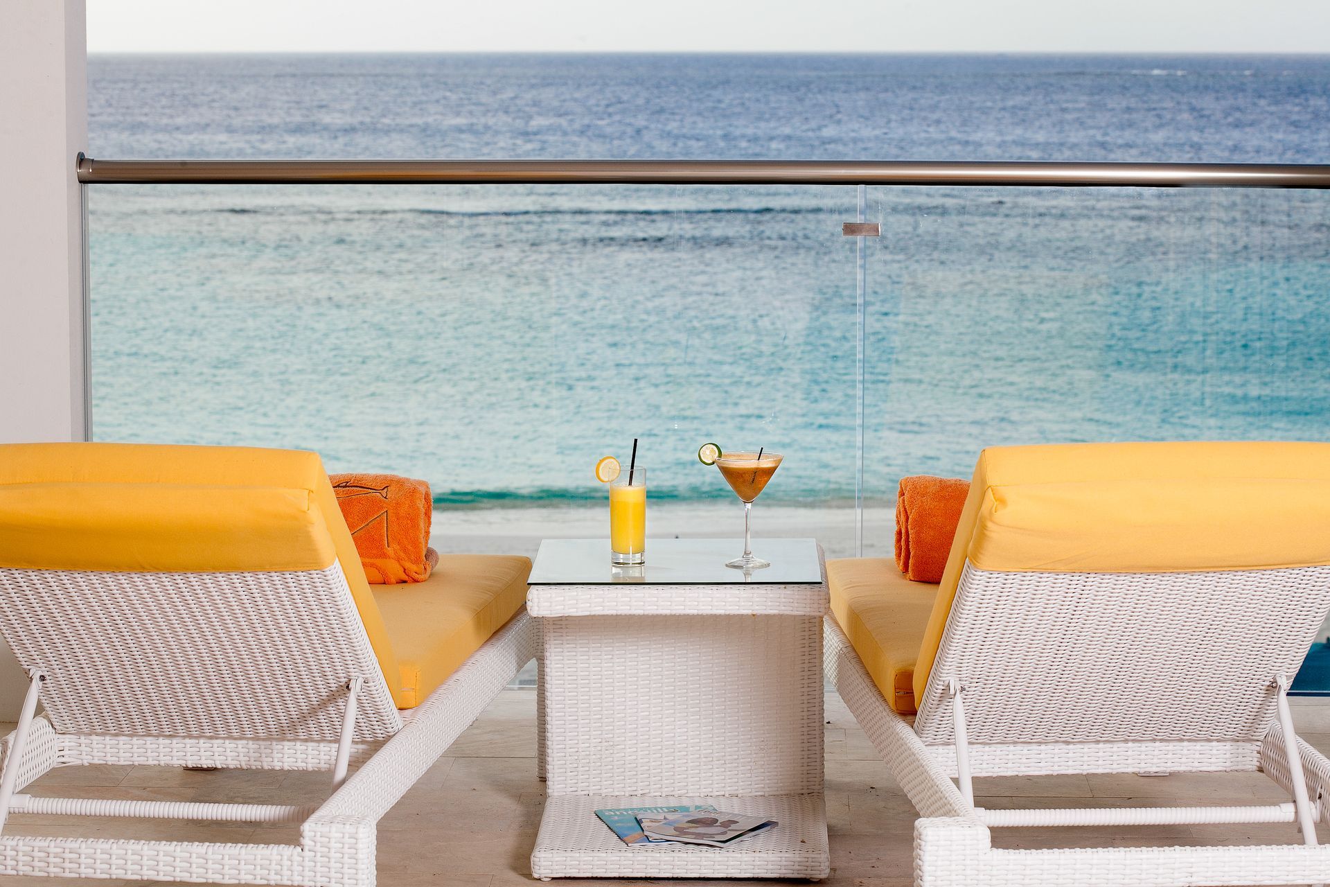 Two lounge chairs with drinks on a table overlooking the ocean.