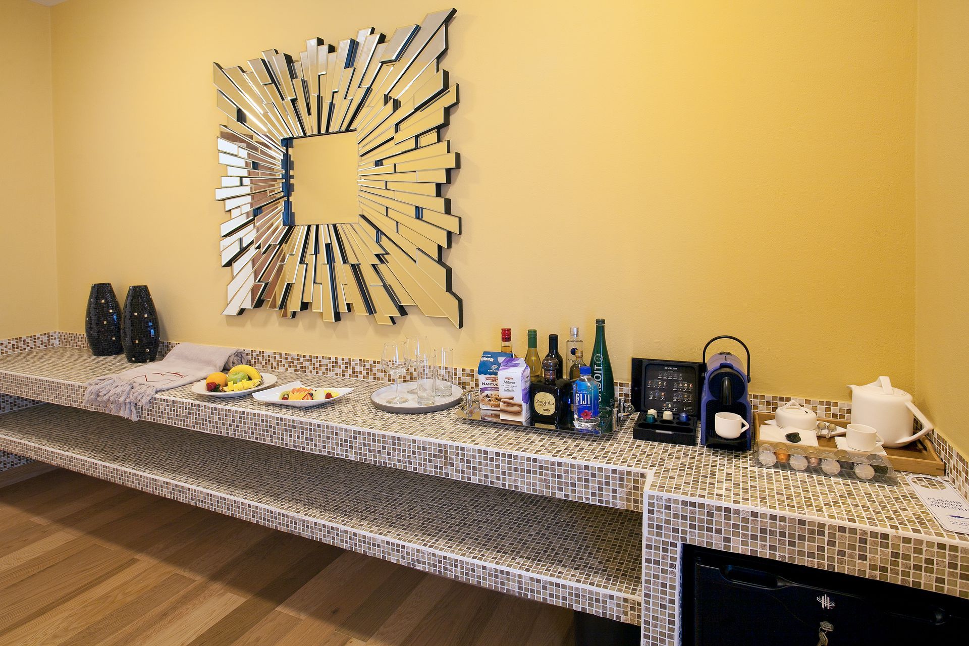 Bar area with snacks, drinks, teapot, and decorative mirror on a mosaic tiled counter.