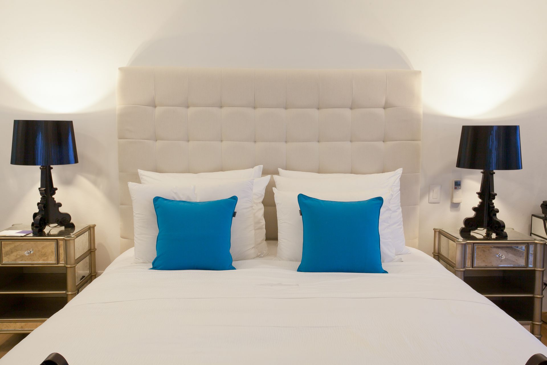 Bedroom with a white bed, two blue pillows, and two black lamps on nightstands.