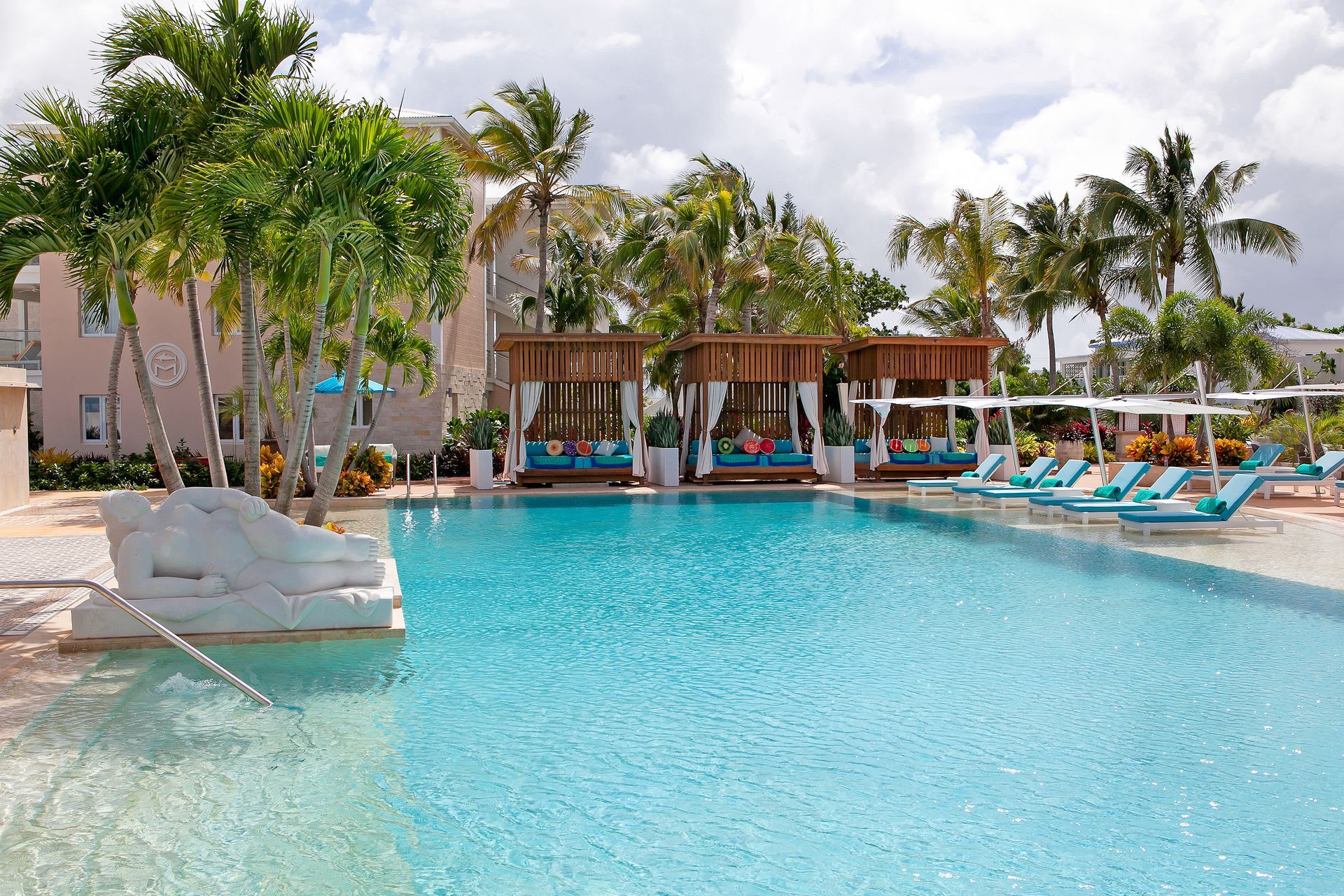 Swimming pool with blue water, cabanas, lounge chairs, and palm trees.