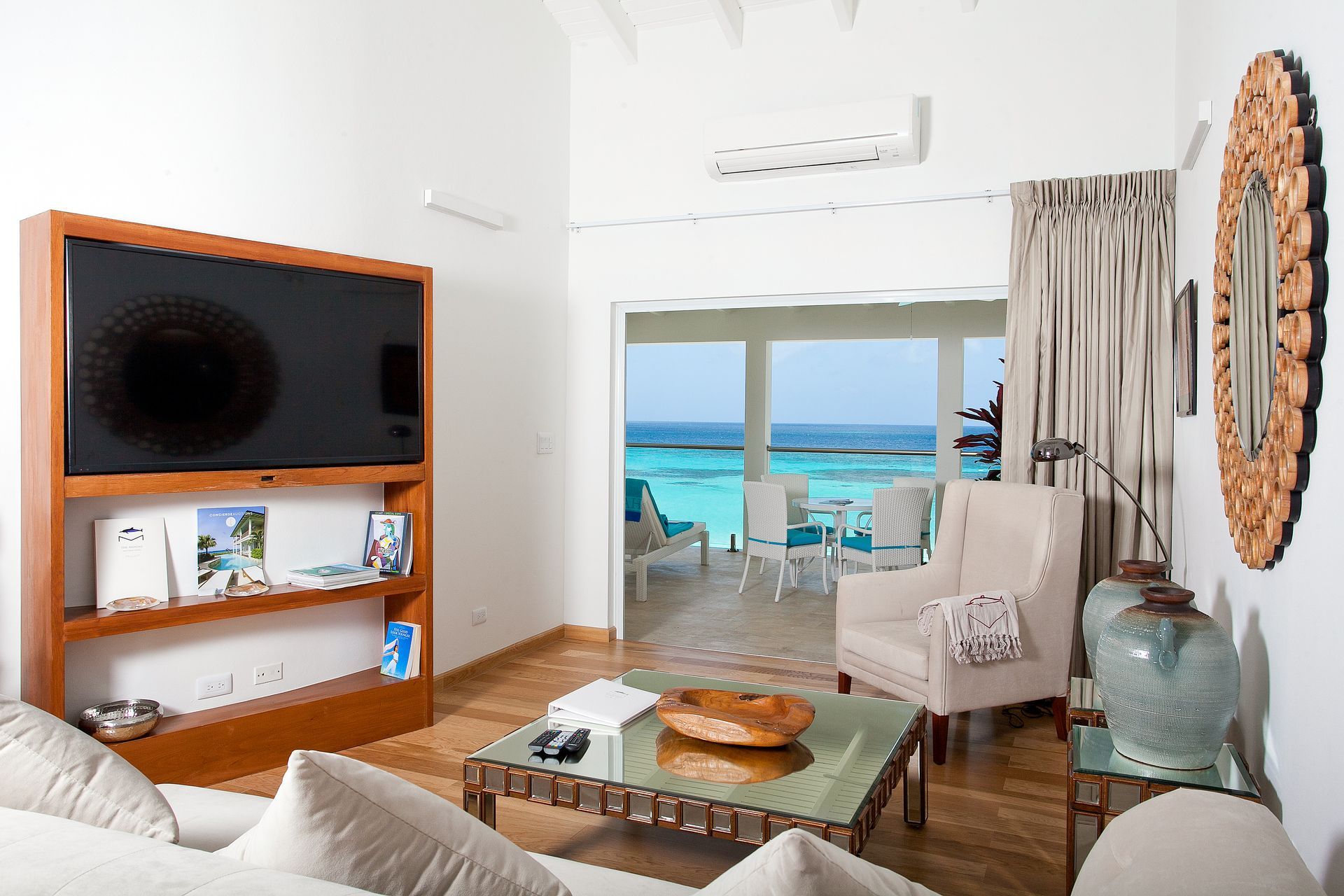 Living room with a large TV, ocean view, and white furniture.