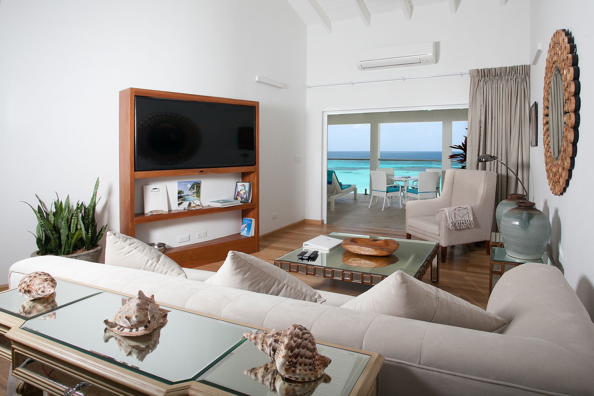 Living room with ocean view, white couch, wooden TV stand, and glass coffee table.