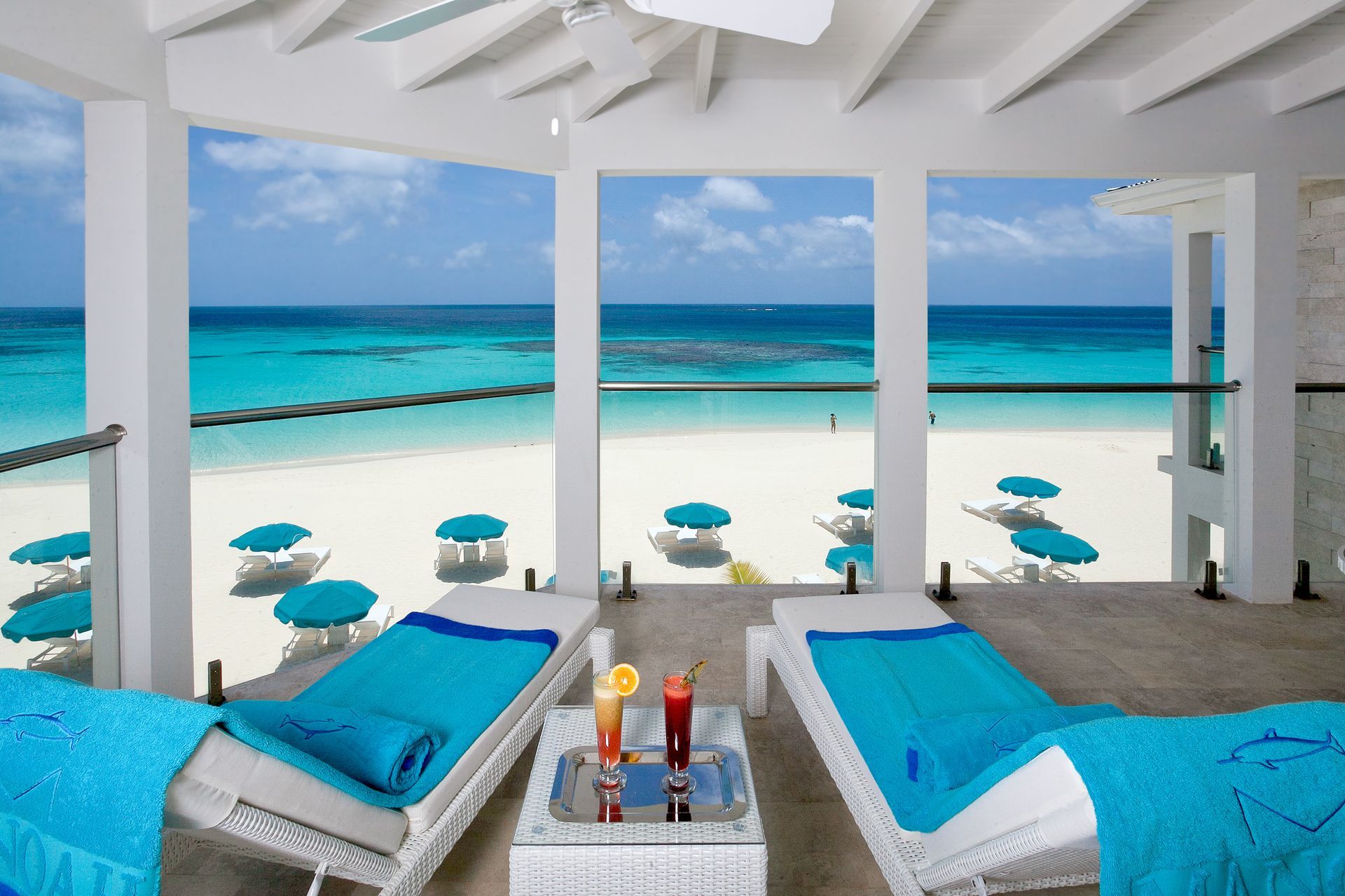 Beach scene with lounge chairs, turquoise towels, drinks, and ocean view.