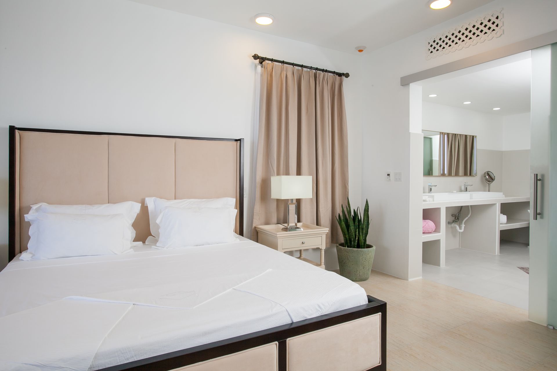 Bedroom with a bed, a nightstand with a lamp, and an open door to a bathroom.