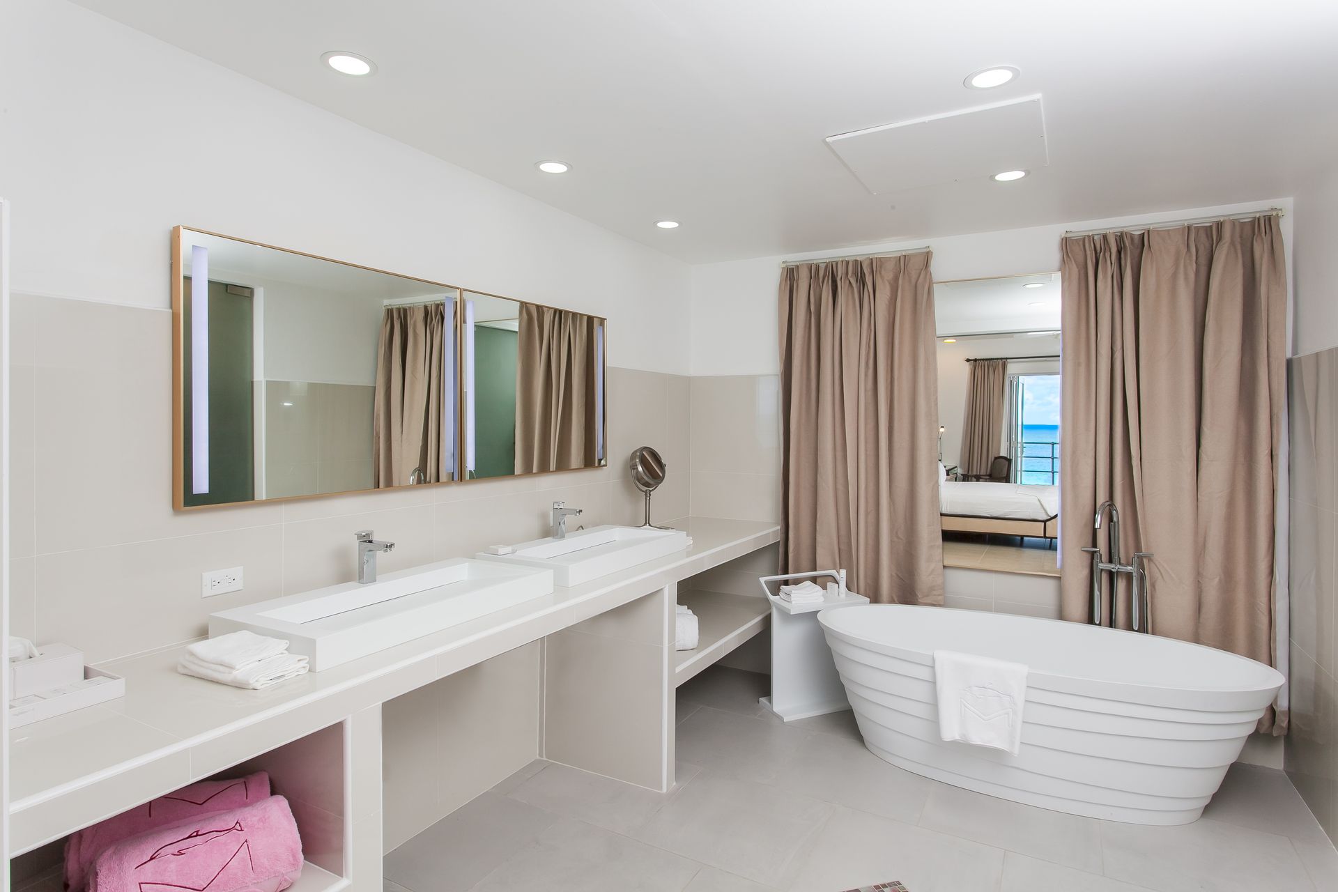 Modern bathroom with a double vanity, soaking tub, and a view of the sea.