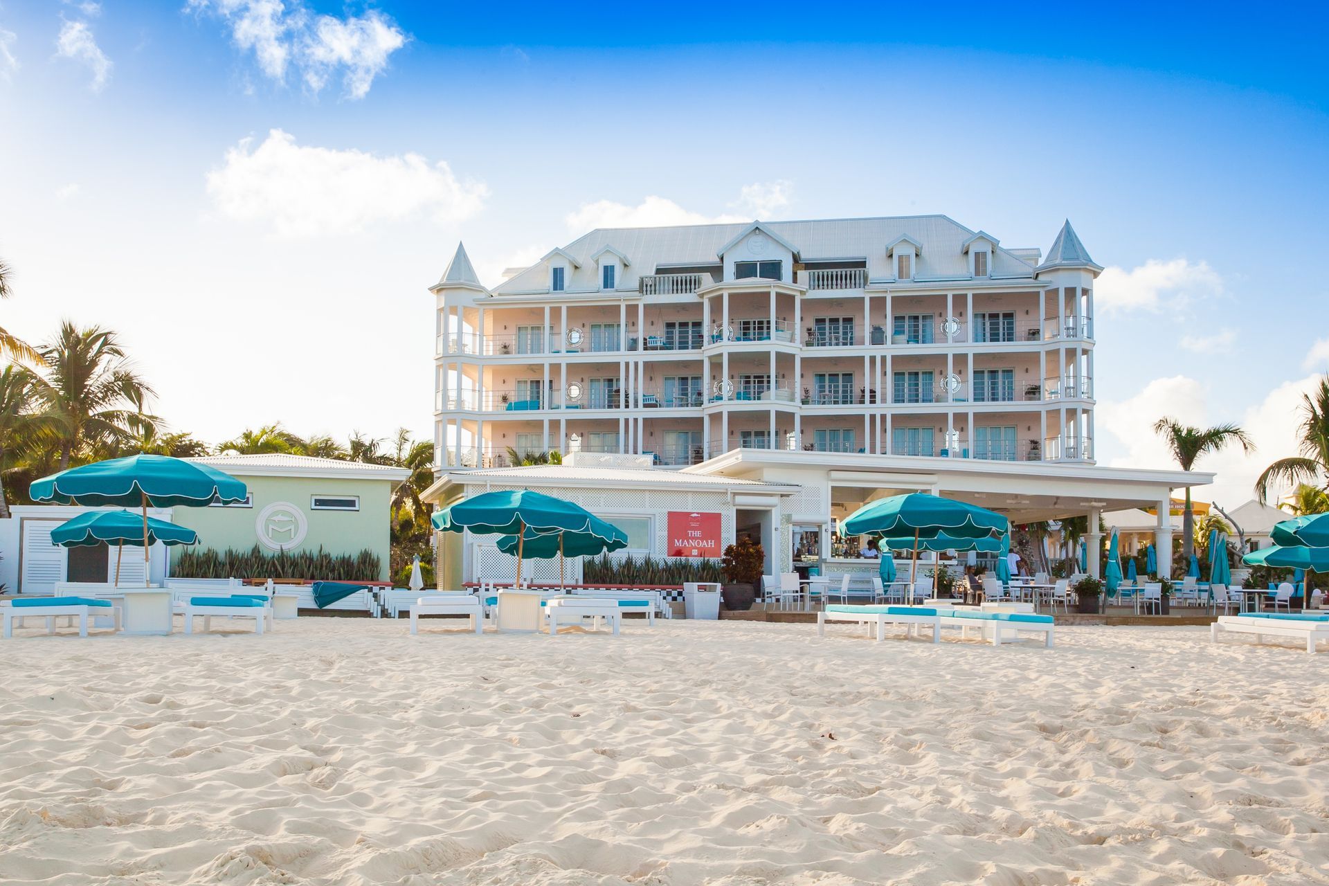 Hotel on white sand beach with turquoise umbrellas and clear blue sky.