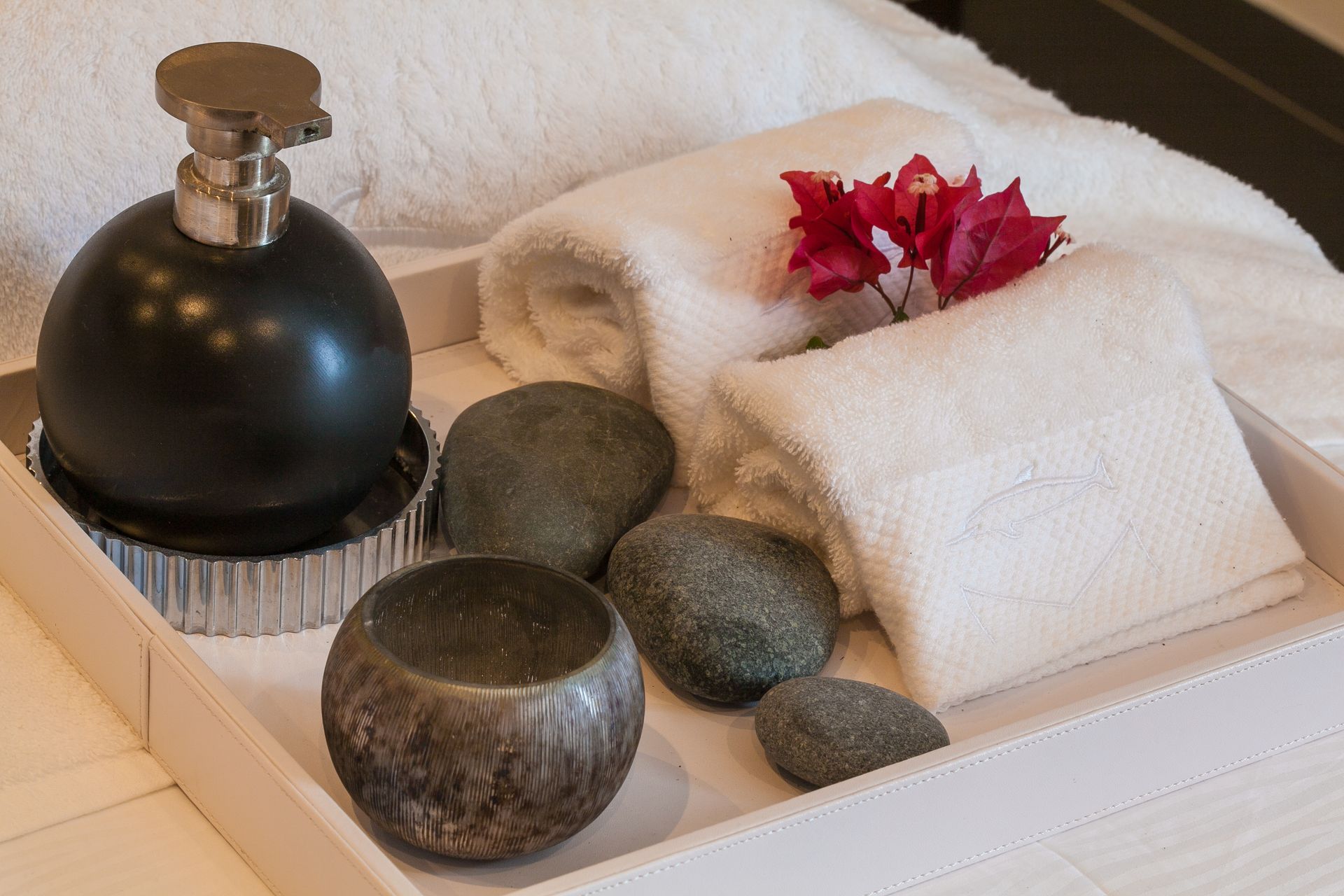 Spa tray with towels, soap dispenser, rocks, and red flowers.