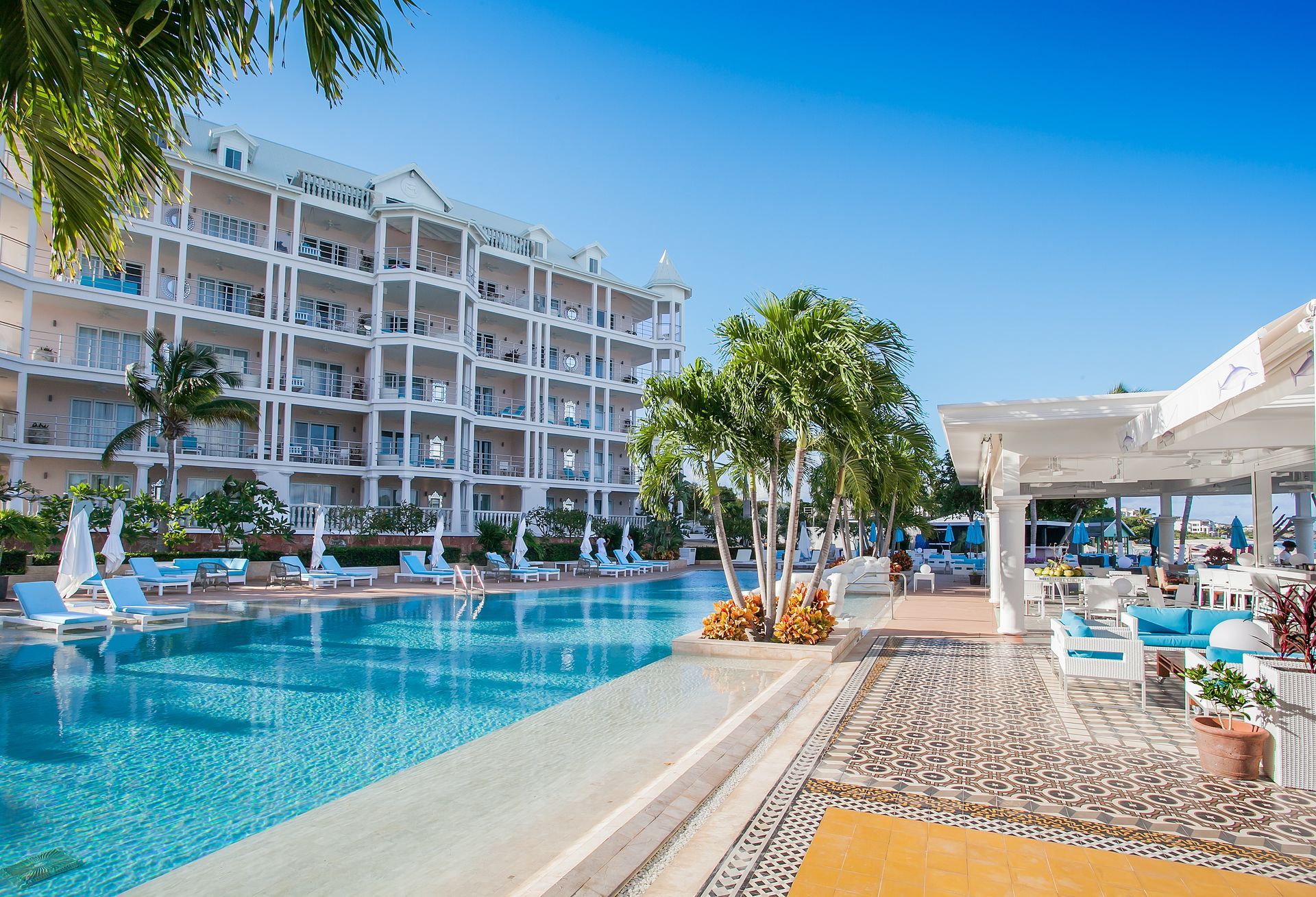 Poolside resort with white building, blue pool, and sunny sky.