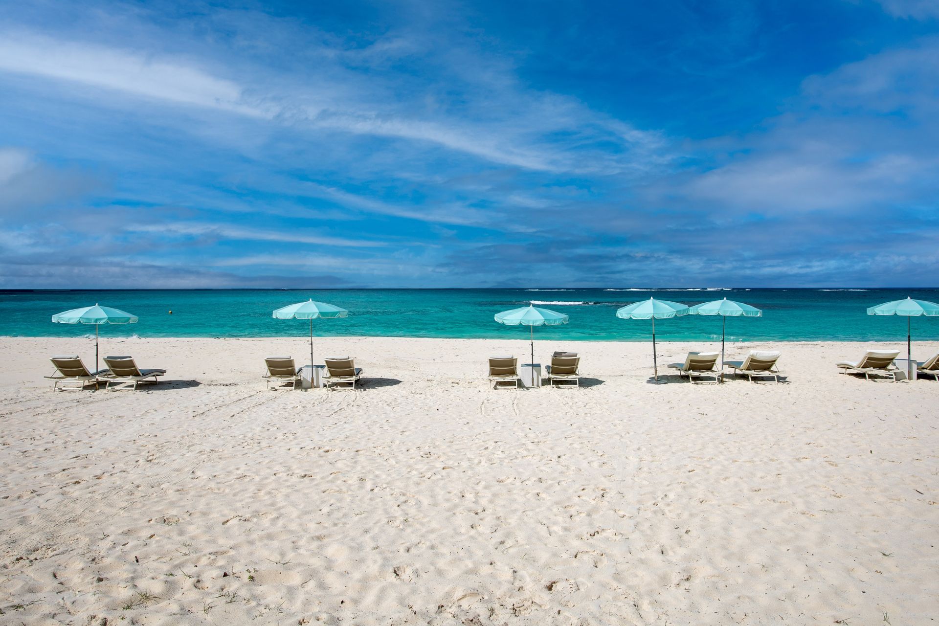White sand beach with turquoise water, lounge chairs, and blue umbrellas under a blue sky.