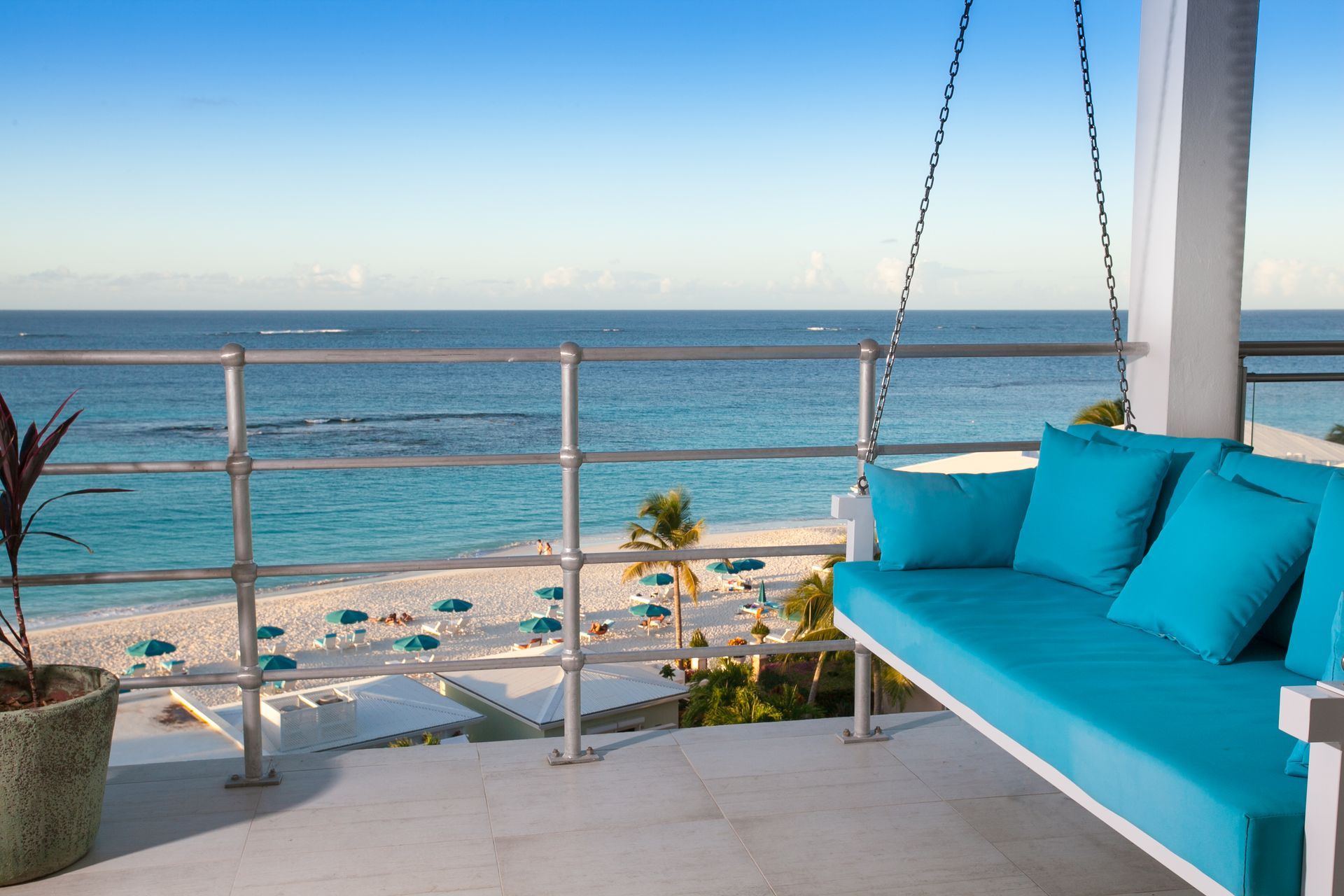 Balcony overlooking a white sand beach and turquoise ocean, featuring a blue swing seat.