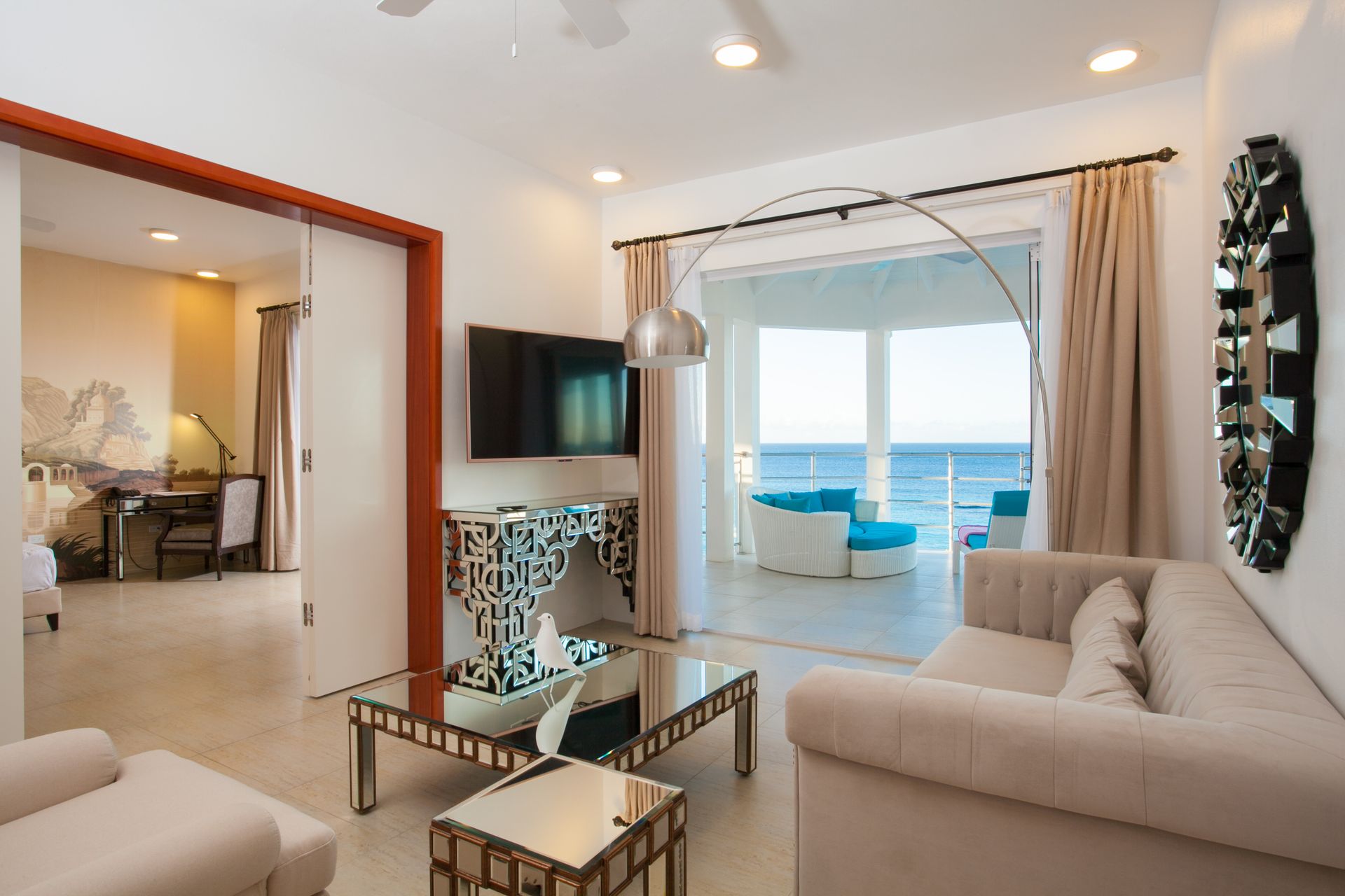 Living room with a view of the ocean. A modern, bright space with a balcony, beige furniture, and large windows.