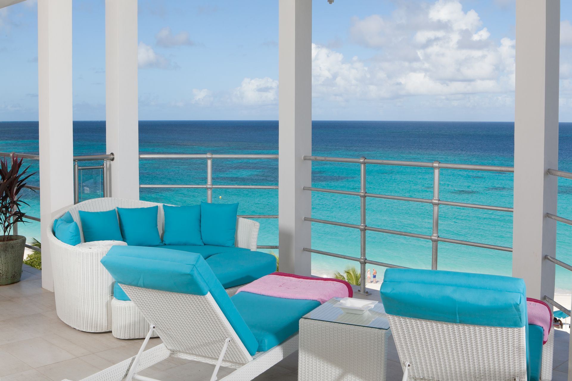 White outdoor seating with turquoise cushions overlooking a blue ocean.