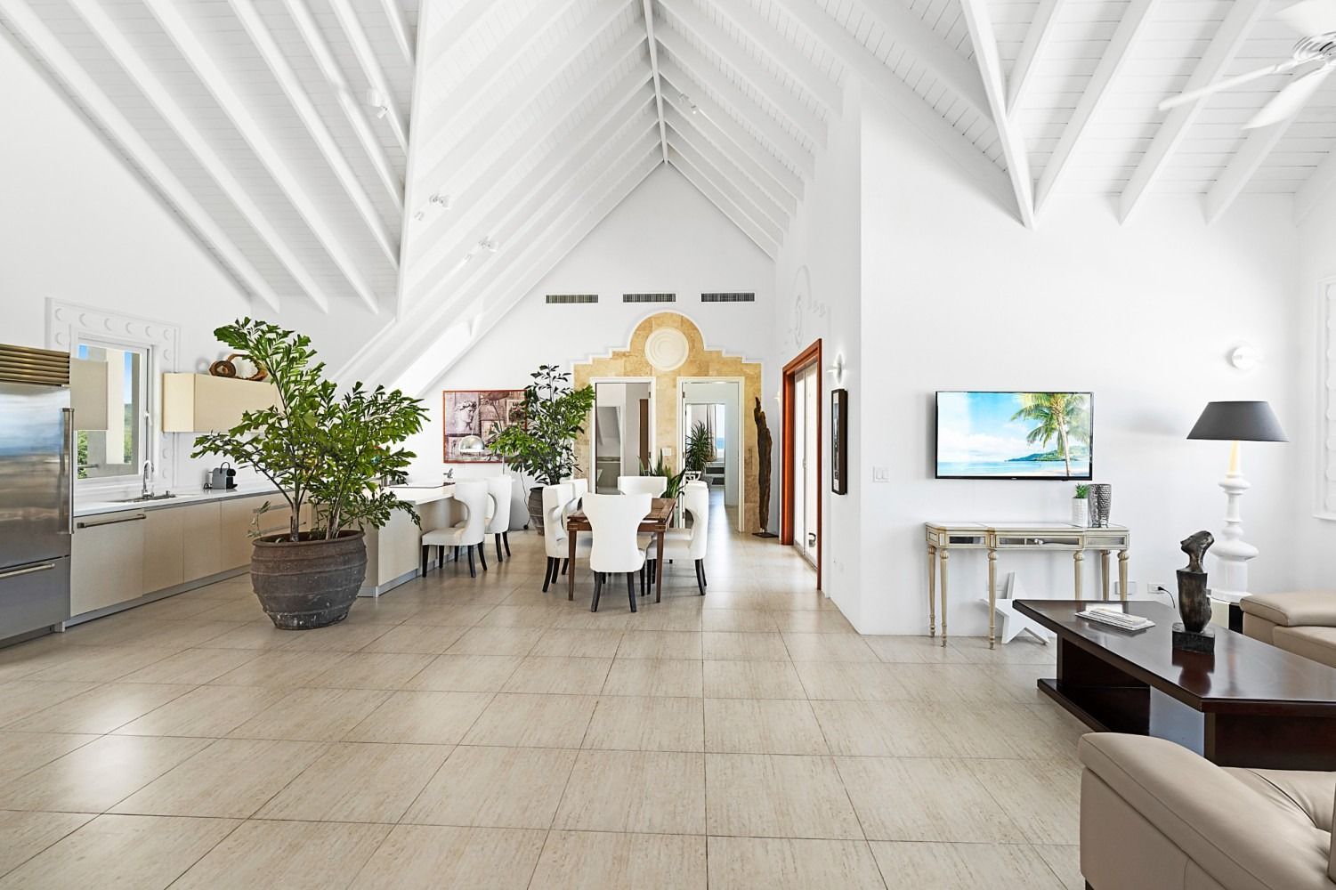 Bright, spacious white-walled living space with cathedral ceiling; includes kitchen, dining area, and lounge area with TV.