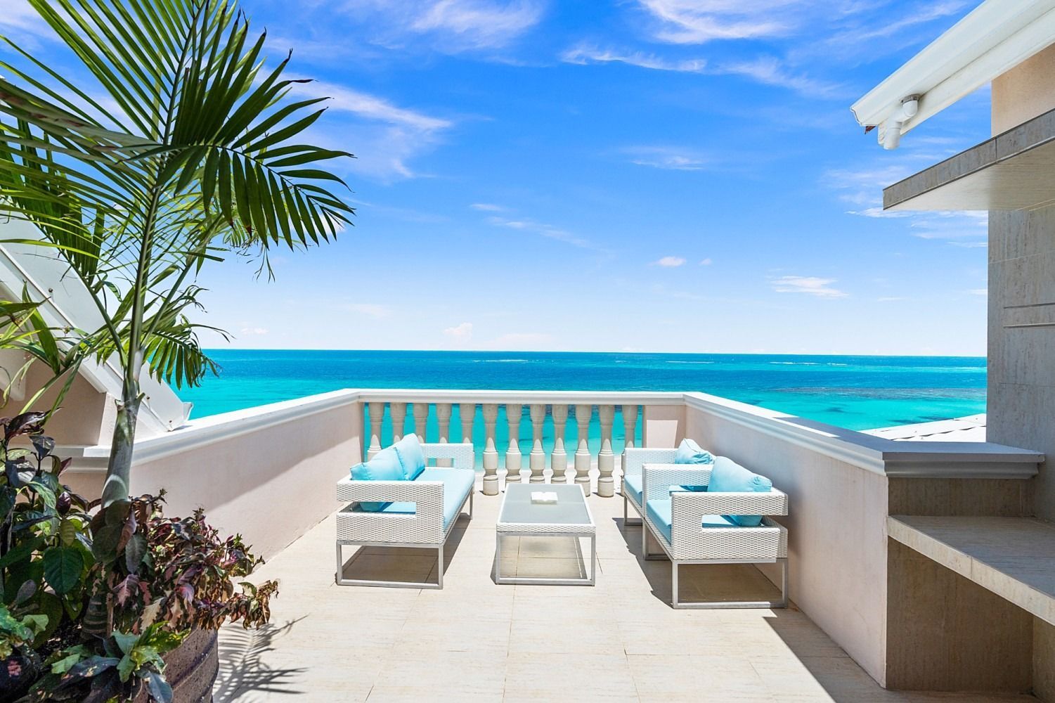 Balcony overlooking turquoise ocean with white furniture and a blue sky.