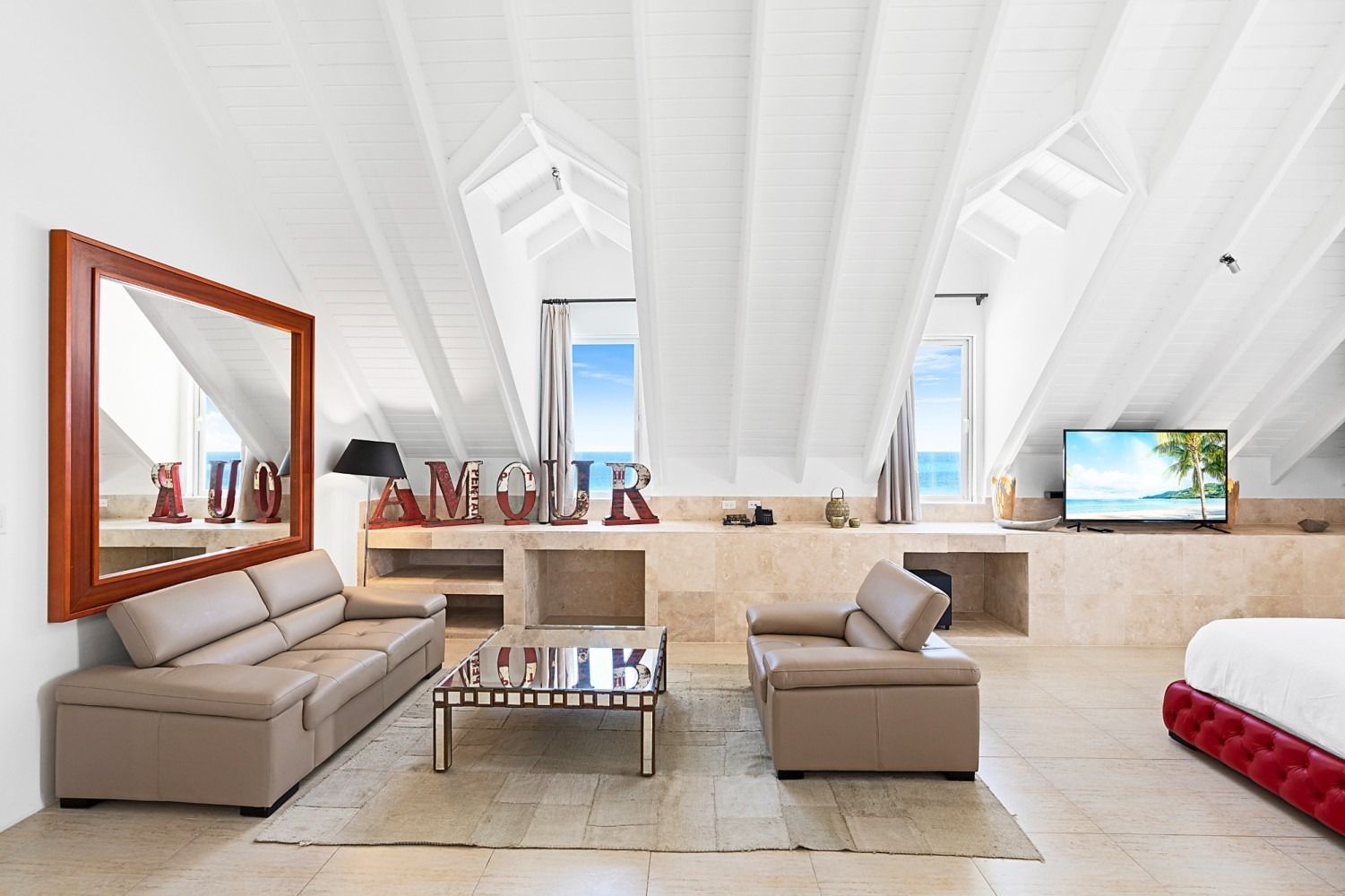 Bright attic living room with couches, mirror, coffee table, windows, and TV.