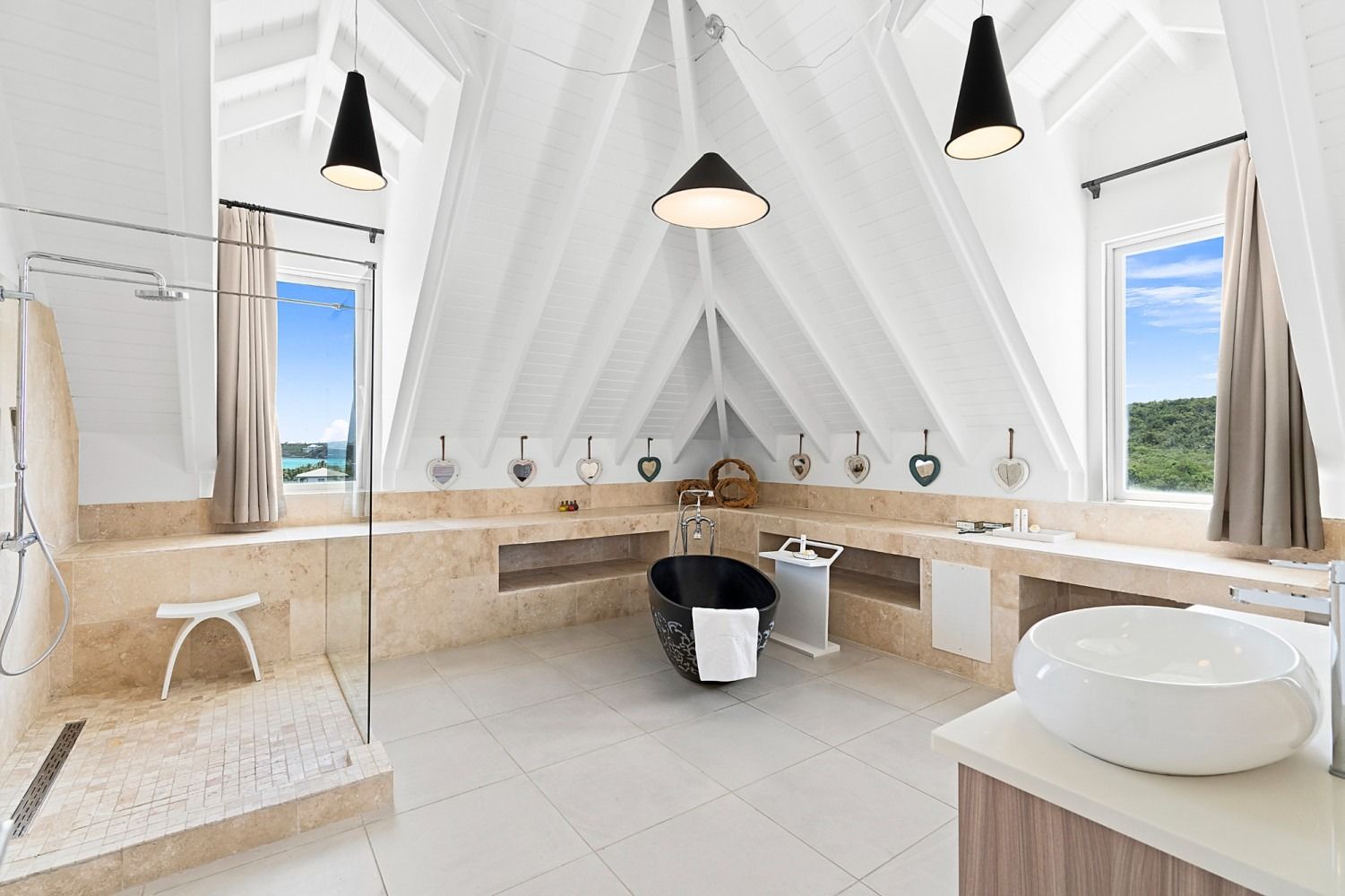 Spacious luxury bathroom with vaulted ceiling, black tub, glass shower, and large windows overlooking scenery.