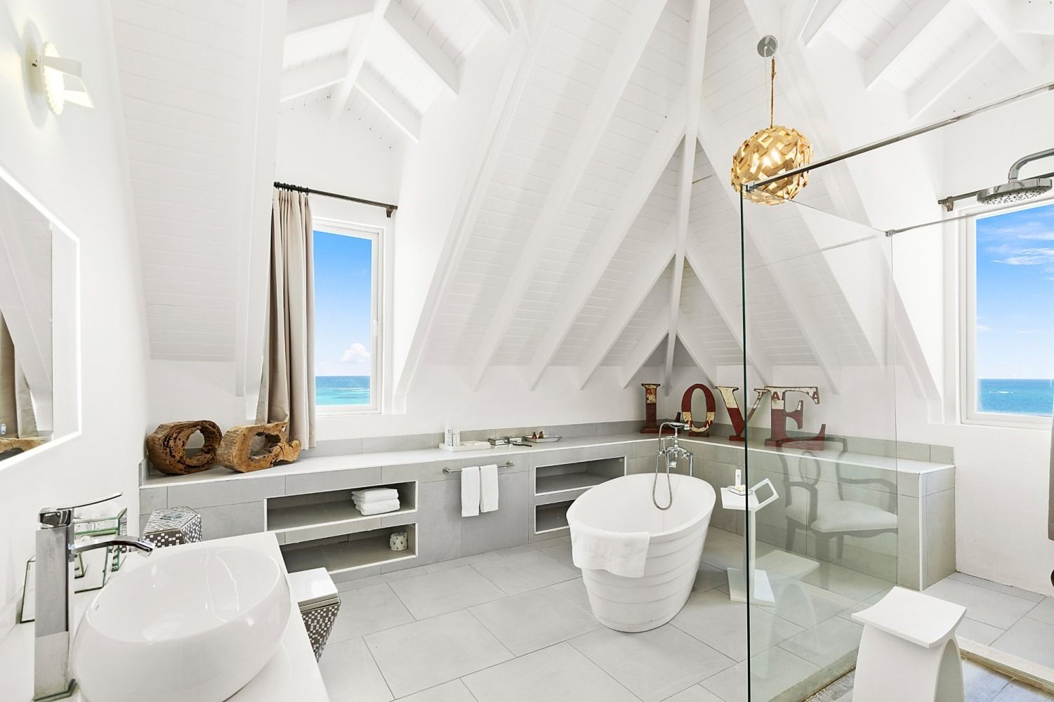 Bright, white bathroom with a freestanding tub, glass shower, and ocean views.