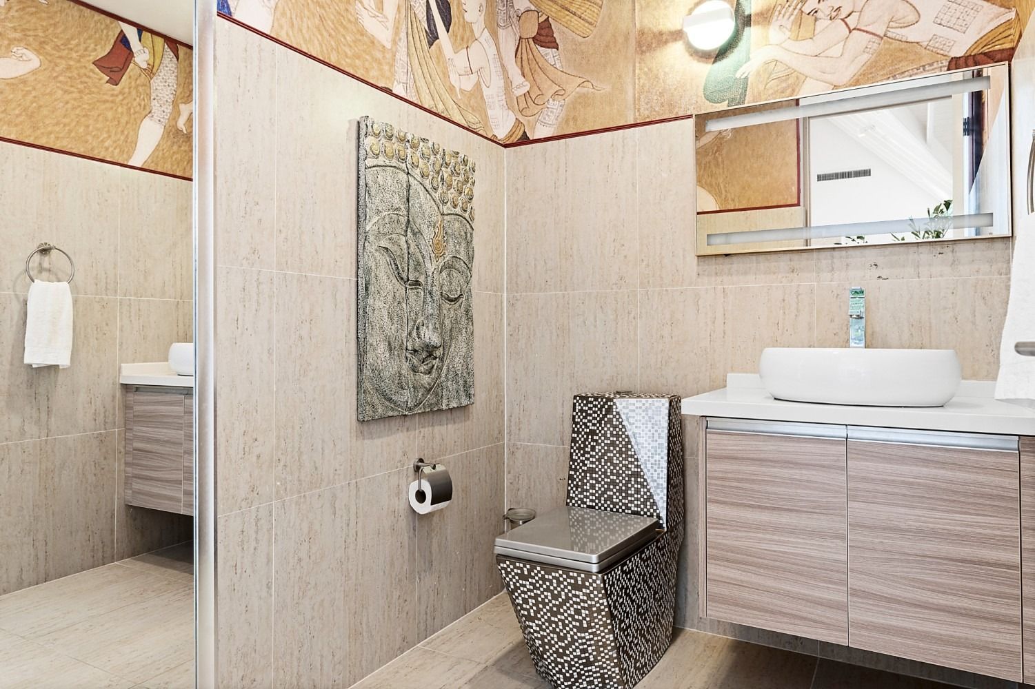 Bathroom with tan tile walls, mosaic accent, and a decorative toilet.