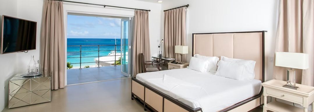 A bedroom with a bed and ocean view through sliding glass doors.