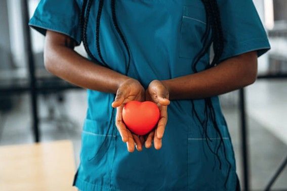 Doctor in blue scrubs holding a brown teddy bear, indoors.