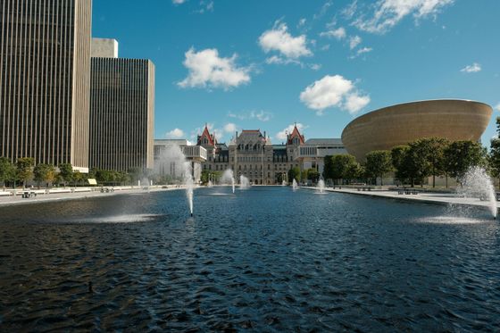 Fountains in a reflecting pool with the New York State Capitol Building and modernist structures in Albany.