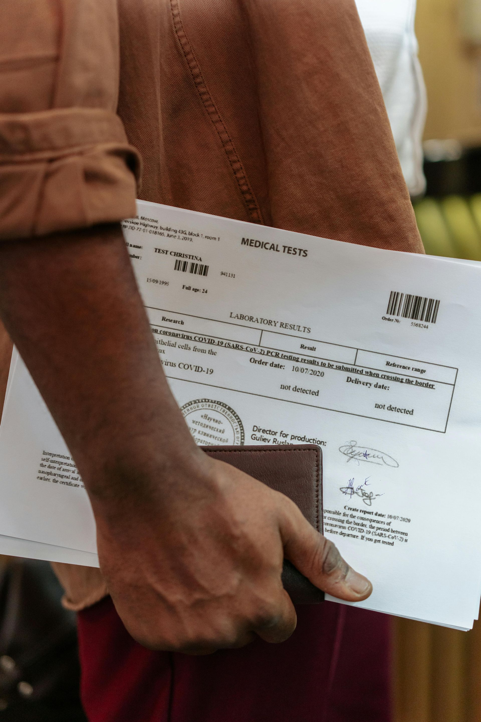 Person holding documents and a wallet, wearing brown clothing; indoors.