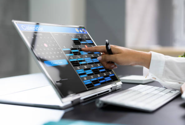 Person pointing at a calendar displayed on a laptop screen, scheduling appointments.