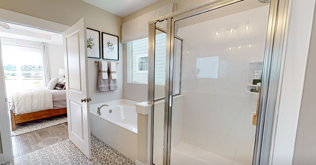 Bathroom with shower, tub, and doorway to bedroom. White and neutral tones, glass shower doors.