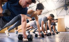 Group of people in a gym doing push-ups with dumbbells.