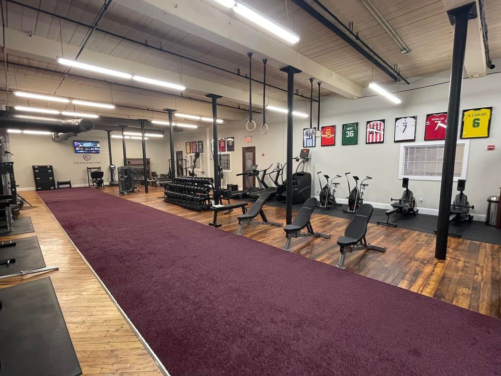 Interior gym with various exercise equipment on hardwood floors and a red turf running lane.
