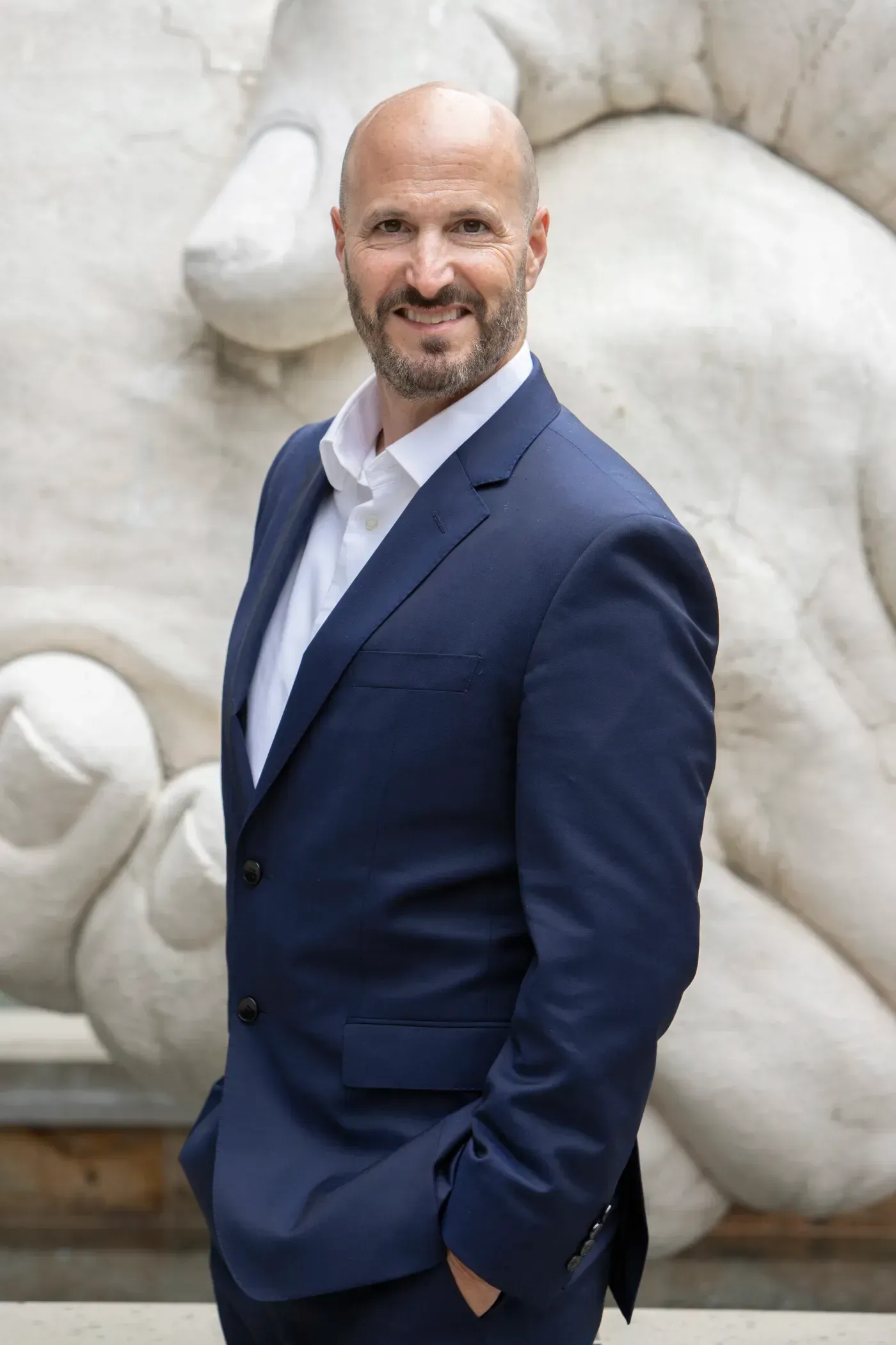 A man in a suit and white shirt is standing in front of a statue of a lion.