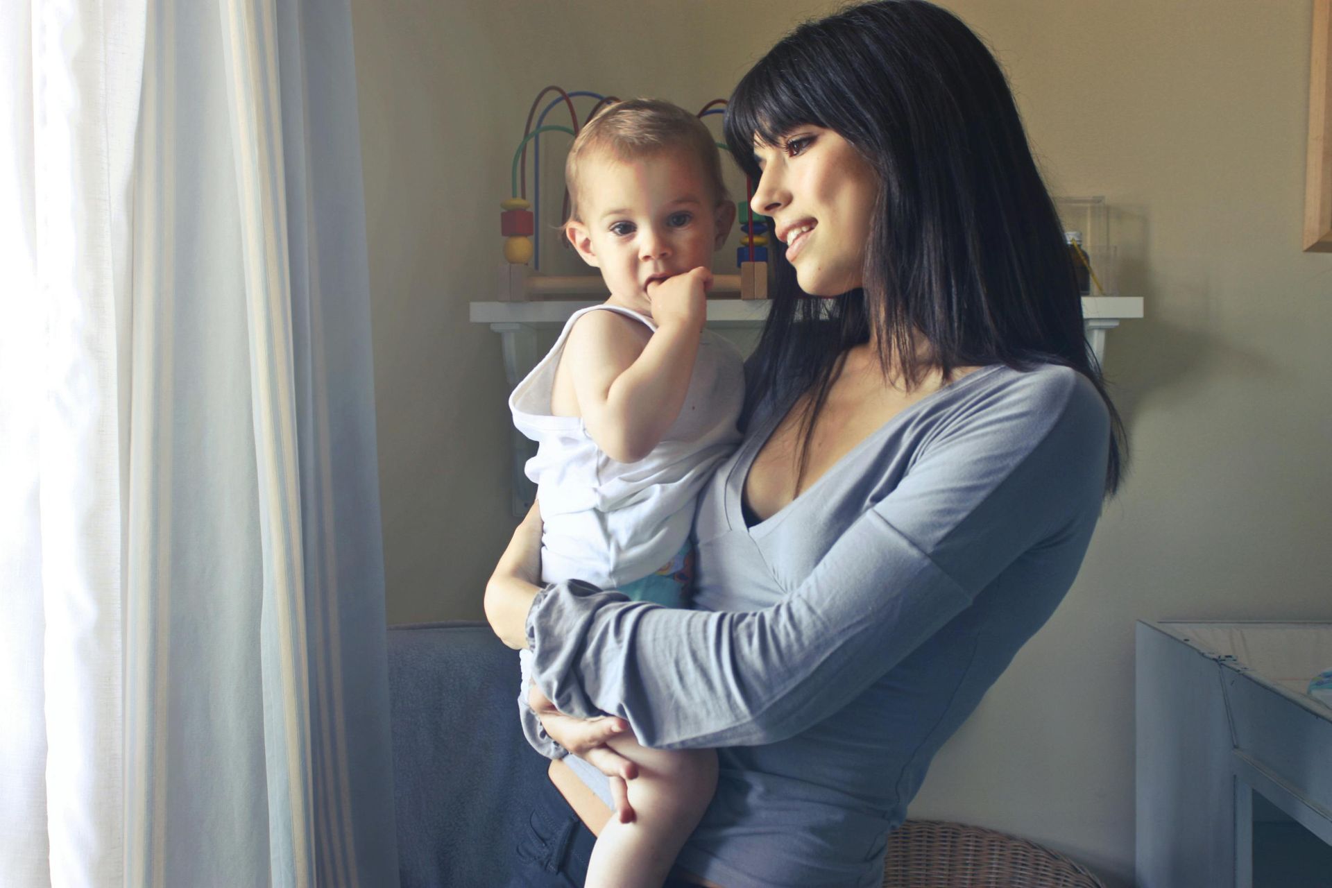 Woman holding child by window in nursery