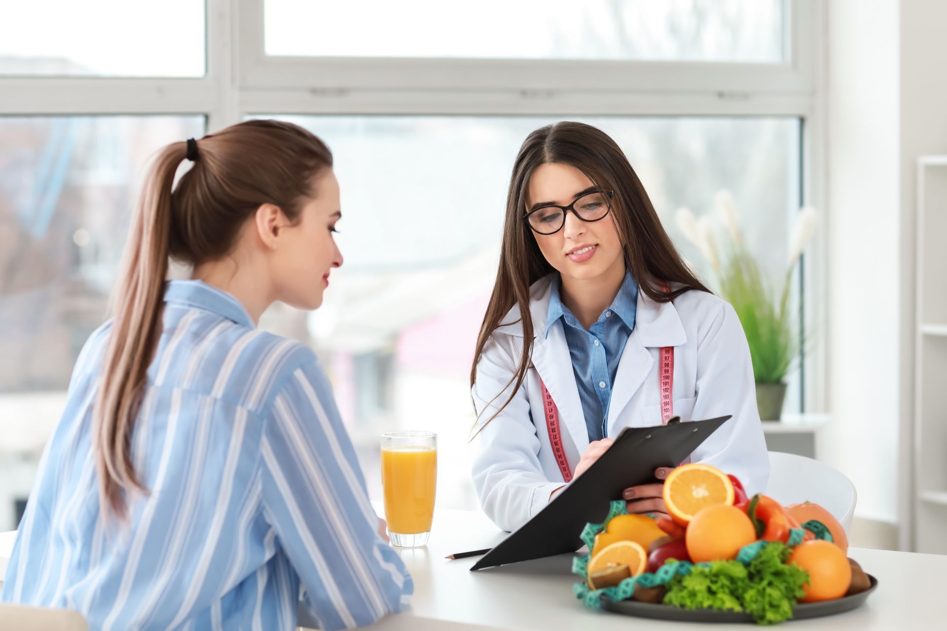 A woman consults with a dietitian, who is taking notes. A plate of fruit sits on the table.