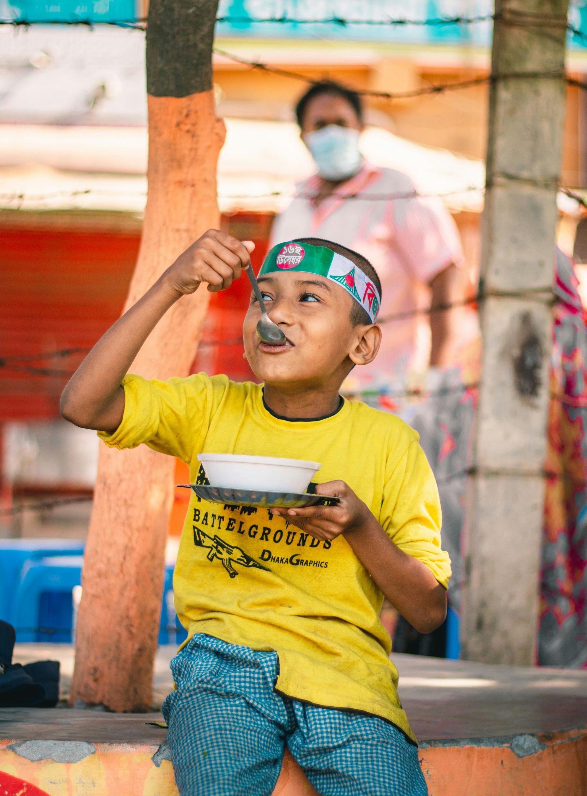 A young boy is sitting on a bench eating food from a bowl.