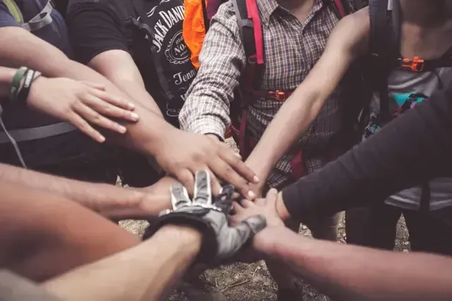 A group of people are putting their hands together in a circle demonstrating SDL's collaboration With Local Businesses.