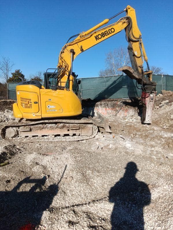 A yellow kobelco excavator is digging a hole in the dirt.