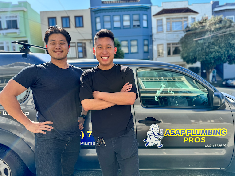 Two men are standing in front of a plumbing truck.