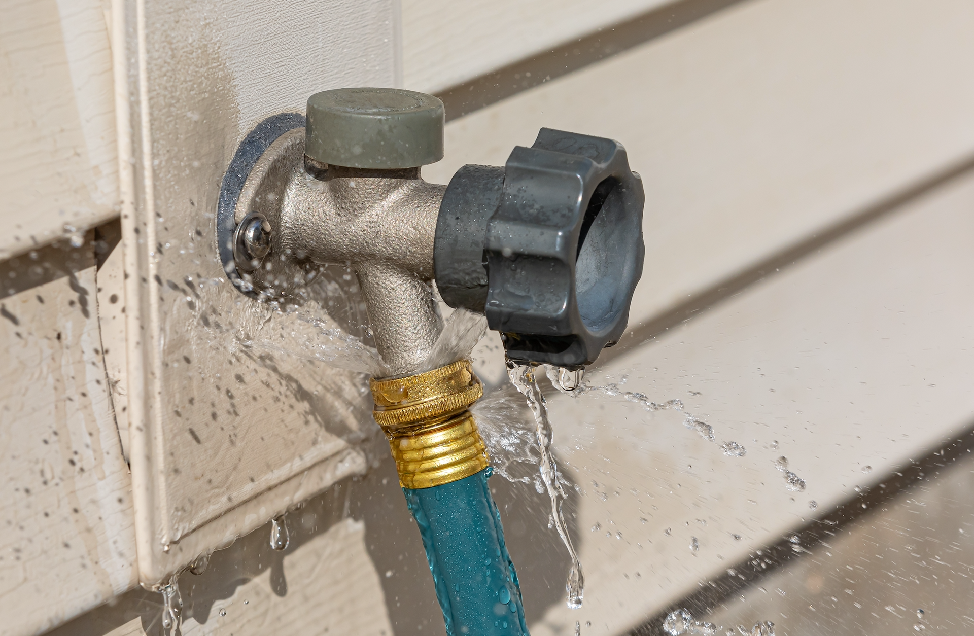 A hose is leaking water from a faucet on a wall.