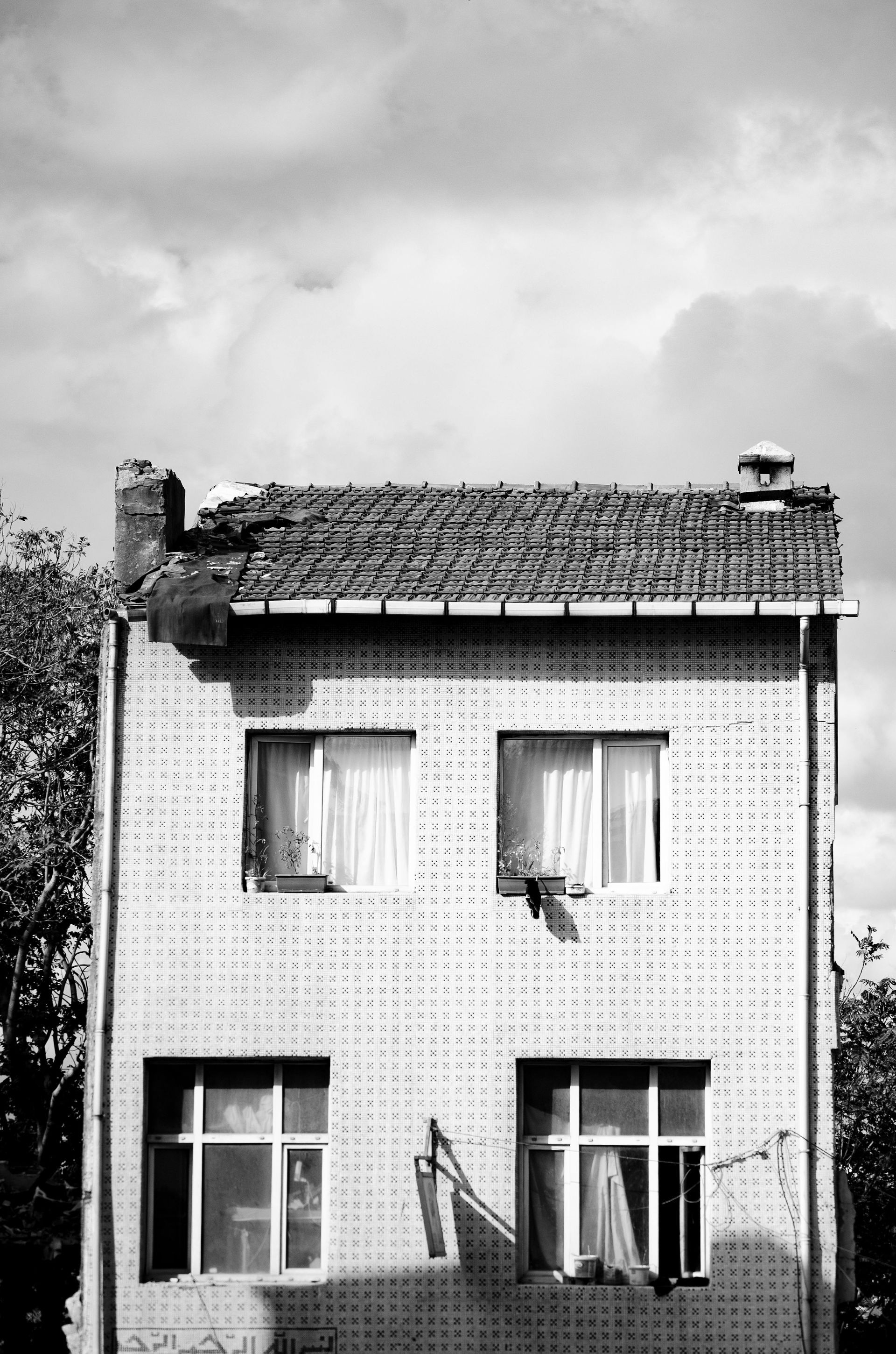 Brick building with four windows, roof tiles, and a cloudy sky in black and white.