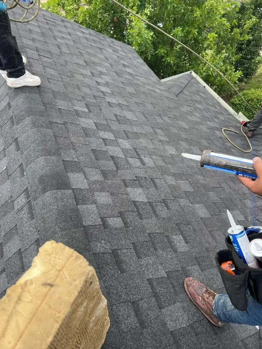 Person applying sealant to a dark gray shingle roof.