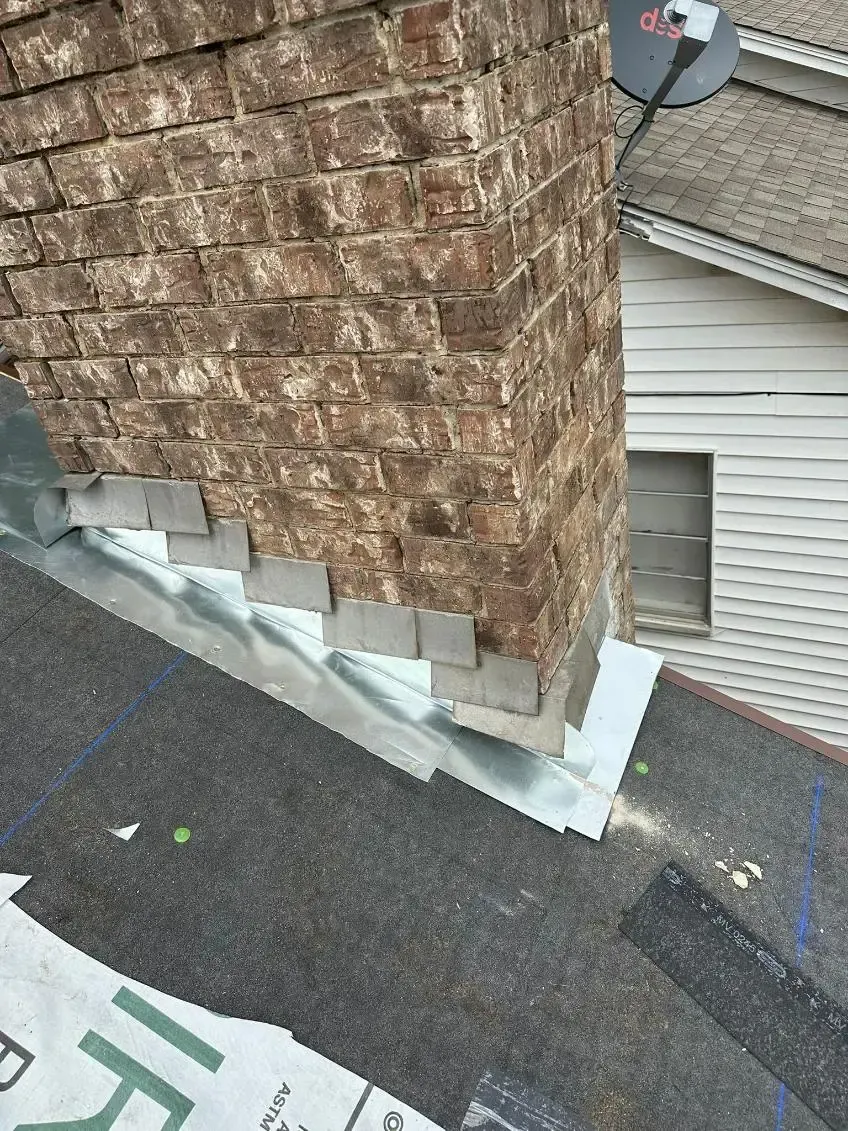 Brick chimney with new metal flashing on a dark shingle roof.