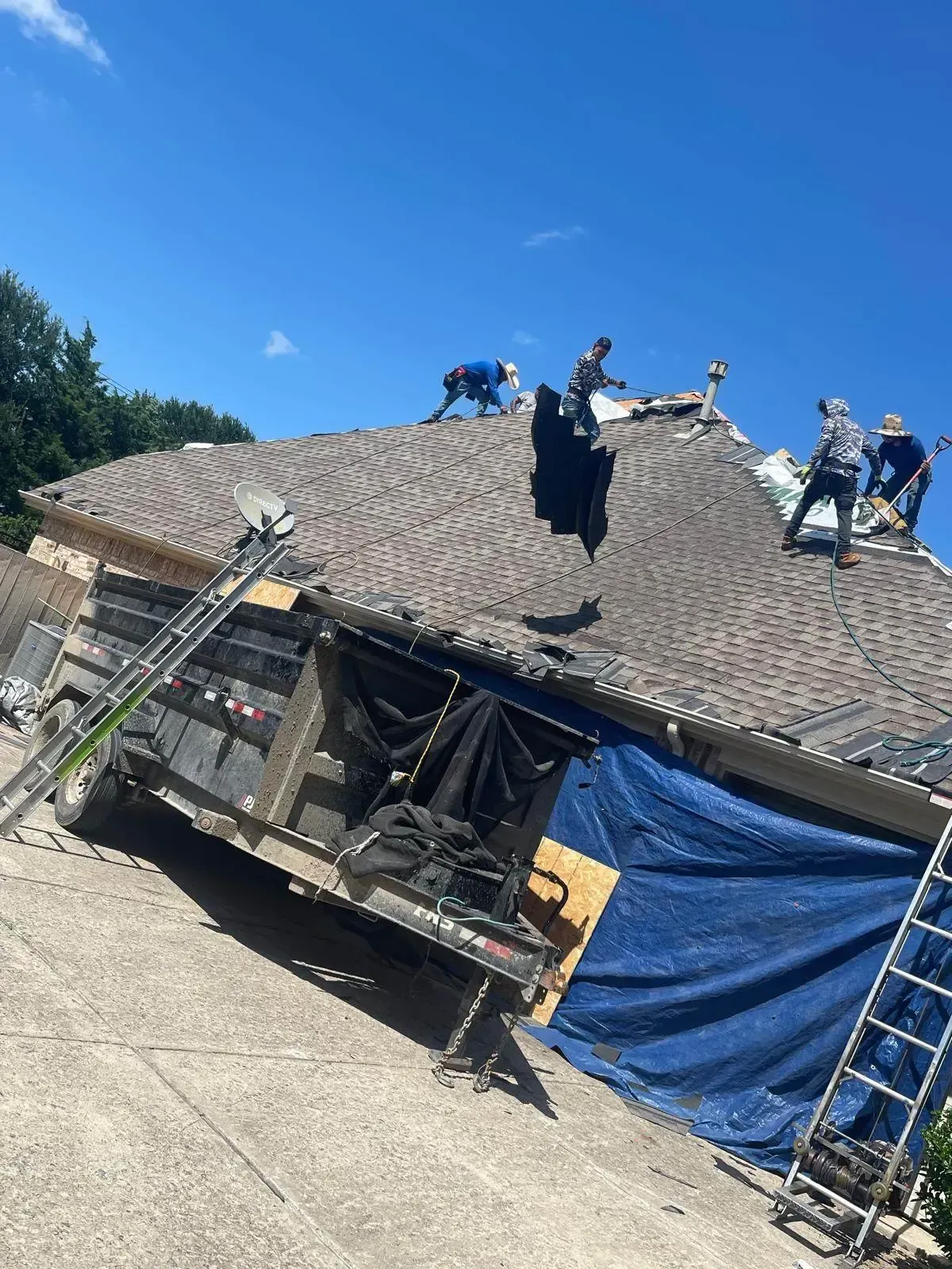 Roofers working on a house roof on a sunny day. A truck with tarp is on the driveway.